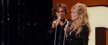 Movie still from “Walk Hard: The Dewey Cox Story” (2007), directed by Jake Kasdan – A man and a woman sing into microphones; Medium shot, Over the shoulder angle