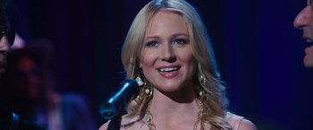 Movie still from “Walk Hard: The Dewey Cox Story” (2007), directed by Jake Kasdan – A beautiful blonde woman holding a microphone; Close Up shot, Over the shoulder angle