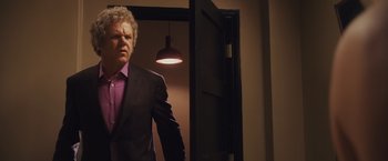 Movie still from “Walk Hard: The Dewey Cox Story” (2007), directed by Jake Kasdan – A man in a suit and tie standing in front of an open door; Medium shot, Low angle