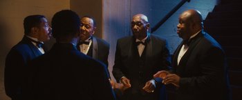 Movie still from “Walk Hard: The Dewey Cox Story” (2007), directed by Jake Kasdan – A man in a tuxedo is talking to two other men; Medium shot, Over the shoulder angle