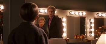 Movie still from “Walk Hard: The Dewey Cox Story” (2007), directed by Jake Kasdan – A man in a black suit is looking at himself in the mirror; Medium shot, Over the shoulder angle