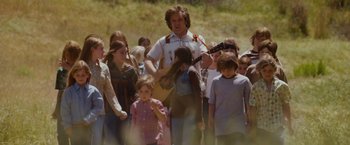 Movie still from “Walk Hard: The Dewey Cox Story” (2007), directed by Jake Kasdan – A group of people standing in a field with a man holding a guitar; Wide shot, Over the shoulder angle