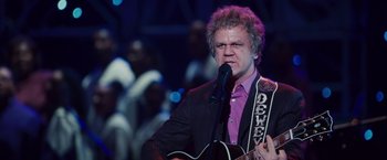 Movie still from “Walk Hard: The Dewey Cox Story” (2007), directed by Jake Kasdan – A man in a purple shirt is holding a guitar; Close Up shot, Low angle