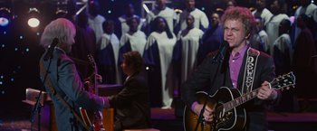 Movie still from “Walk Hard: The Dewey Cox Story” (2007), directed by Jake Kasdan – A group of people in a room with guitars and instruments; Medium shot, Over the shoulder angle