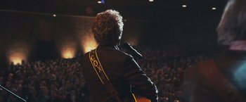 Movie still from “Walk Hard: The Dewey Cox Story” (2007), directed by Jake Kasdan – A man with a microphone and a guitar in front of an audience; Medium shot, Over the shoulder angle