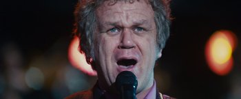 Movie still from “Walk Hard: The Dewey Cox Story” (2007), directed by Jake Kasdan – An older man with a beard is singing into a microphone; Close Up shot, Low angle