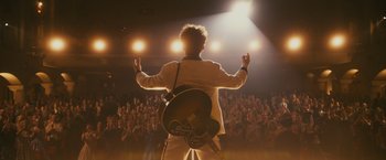 Movie still from “Walk Hard: The Dewey Cox Story” (2007), directed by Jake Kasdan – A man holding a guitar in front of an audience; Wide shot, Low angle