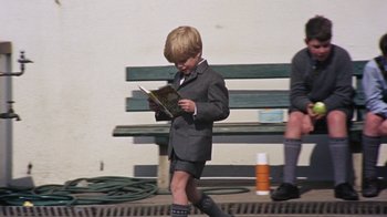 Movie still from “Walkabout” (1971), directed by Nicolas Roeg – A young boy in a suit is reading a book on a bench; Wide shot, High angle