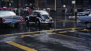 Movie still from “Walkabout” (1971), directed by Nicolas Roeg – An old car driving down a street in the rain; Extreme Wide shot, High angle