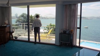 Movie still from “Walkabout” (1971), directed by Nicolas Roeg – A man standing in front of a window looking out at the ocean; Wide shot, High angle