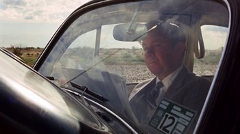 Movie still from “Walkabout” (1971), directed by Nicolas Roeg – An older man sitting in the passenger seat of a car; Medium shot, Over the shoulder angle