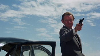 Movie still from “Walkabout” (1971), directed by Nicolas Roeg – A man standing next to a car on the side of the road; Medium shot, Low angle
