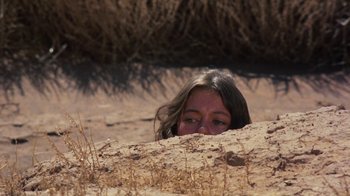 Movie still from “Walkabout” (1971), directed by Nicolas Roeg – A woman is hiding in the sand in the desert; Medium shot, High angle