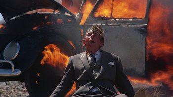 Movie still from “Walkabout” (1971), directed by Nicolas Roeg – A man sitting in front of a burning building; Medium shot, Low angle