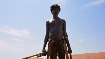 Movie still from “Walkabout” (1971), directed by Nicolas Roeg – A man standing in the sand holding a stick; Wide shot, Low angle