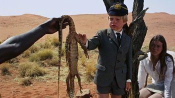 Movie still from “Walkabout” (1971), directed by Nicolas Roeg – A young boy in a suit holding a lizard; Medium shot, Over the shoulder angle