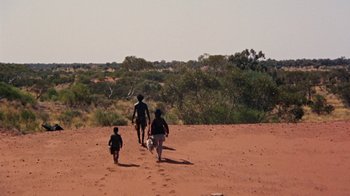 Movie still from “Walkabout” (1971), directed by Nicolas Roeg – A man and two children walking across a dirt field; Extreme Wide shot, High angle