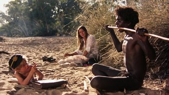 Movie still from “Walkabout” (1971), directed by Nicolas Roeg – A woman sitting on the ground next to two men; Wide shot, Over the shoulder angle