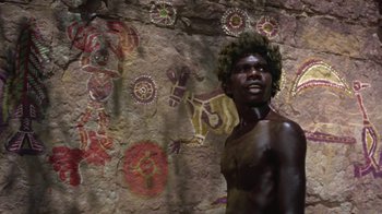 Movie still from “Walkabout” (1971), directed by Nicolas Roeg – A man standing in front of a wall with paintings on it; Medium shot, High angle