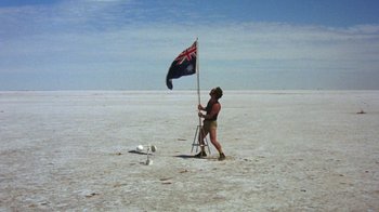 Movie still from “Walkabout” (1971), directed by Nicolas Roeg – A man standing in the middle of a desert holding a flag; Wide shot, Low angle