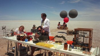 Movie still from “Walkabout” (1971), directed by Nicolas Roeg – A group of people standing around a table; Extreme Wide shot, High angle