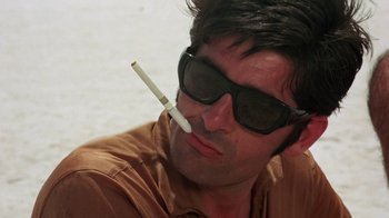 Movie still from “Walkabout” (1971), directed by Nicolas Roeg – A man wearing sunglasses and holding a cigarette in his mouth; Close Up shot, Low angle