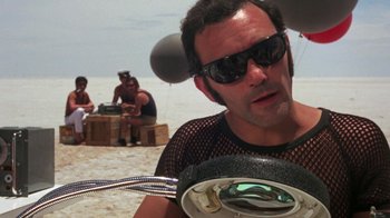 Movie still from “Walkabout” (1971), directed by Nicolas Roeg – A man in a fishnet shirt holding a fish on a beach; Close Up shot, Low angle