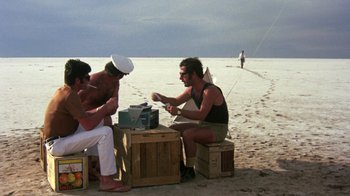 Movie still from “Walkabout” (1971), directed by Nicolas Roeg – A group of men sitting on top of a wooden crate; Wide shot, High angle