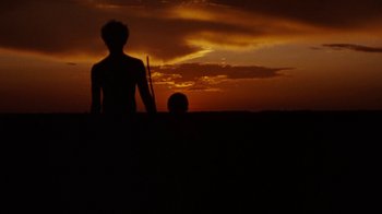 Movie still from “Walkabout” (1971), directed by Nicolas Roeg – A man standing in a field at sunset with a stick; Extreme Wide shot, Low angle