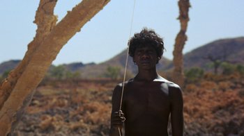 Movie still from “Walkabout” (1971), directed by Nicolas Roeg – A man standing in the middle of a field holding a stick; Medium shot, Low angle