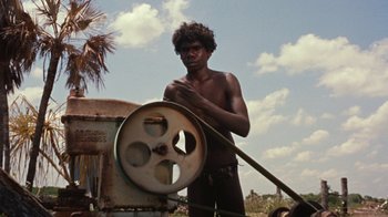 Movie still from “Walkabout” (1971), directed by Nicolas Roeg – A man standing in front of an old machine; Medium shot, High angle