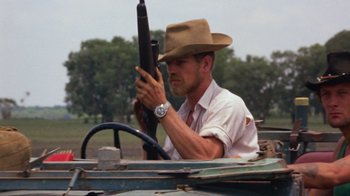 Movie still from “Walkabout” (1971), directed by Nicolas Roeg – A man in a hat holding a rifle in a vehicle; Close Up shot, Over the shoulder angle