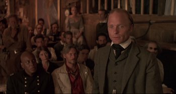 Movie still from “Walker” (1987), directed by Alex Cox – A man in a suit standing in front of a group of people; Medium shot, Low angle