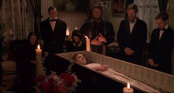 Movie still from “Walker” (1987), directed by Alex Cox – A woman is laying in a casket in front of a group of men; Medium shot, Over the shoulder angle