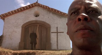 Movie still from “Walker” (1987), directed by Alex Cox – A man standing in front of a building with a cross on it; Close Up shot, Low angle