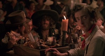 Movie still from “Walker” (1987), directed by Alex Cox – A group of people sitting around a table with food; Close Up shot, Over the shoulder angle