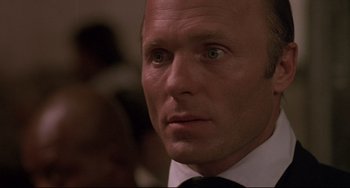 Movie still from “Walker” (1987), directed by Alex Cox – A man in a suit and tie looking at the camera; Close Up shot, Over the shoulder angle