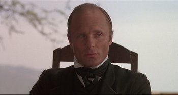 Movie still from “Walker” (1987), directed by Alex Cox – A person sitting in a chair wearing a suit; Close Up shot, Low angle