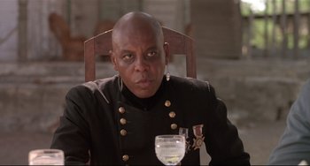 Movie still from “Walker” (1987), directed by Alex Cox – A man sitting in front of a wine glass in a chair; Close Up shot, Low angle