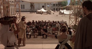 Movie still from “Walker” (1987), directed by Alex Cox – A group of people sitting in front of an audience; Extreme Wide shot, High angle