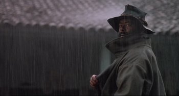 Movie still from “Walker” (1987), directed by Alex Cox – A man in a raincoat holding a stick in the rain; Close Up shot, Low angle