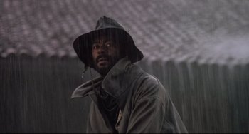 Movie still from “Walker” (1987), directed by Alex Cox – A man in a raincoat under an umbrella in the rain; Close Up shot, Low angle