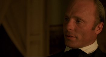 Movie still from “Walker” (1987), directed by Alex Cox – A person wearing a suit and tie; Close Up shot, Over the shoulder angle