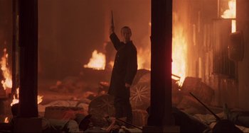 Movie still from “Walker” (1987), directed by Alex Cox – A man holding a gun standing in front of a fire; Medium shot, Low angle