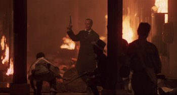 Movie still from “Walker” (1987), directed by Alex Cox – A man holding a gun while standing in front of a fire; Wide shot, Low angle