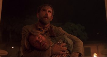 Movie still from “Walker” (1987), directed by Alex Cox – A man holding another man in his arms in the dark; Close Up shot, Low angle