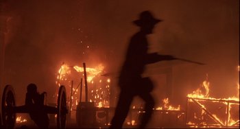 Movie still from “Walker” (1987), directed by Alex Cox – A man in a cowboy hat walking in front of a burning building; Wide shot, Low angle