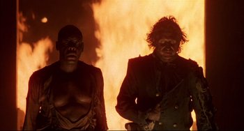 Movie still from “Walker” (1987), directed by Alex Cox – Two men standing next to each other in front of a fire; Medium shot, Low angle