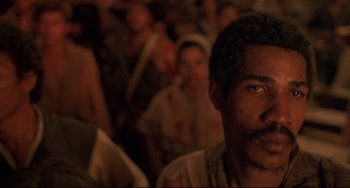 Movie still from “Walker” (1987), directed by Alex Cox – A man's face in front of a group of people; Close Up shot, Over the shoulder angle