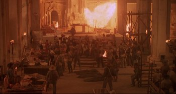 Movie still from “Walker” (1987), directed by Alex Cox – A group of people standing in front of an open fire pit; Extreme Wide shot, High angle